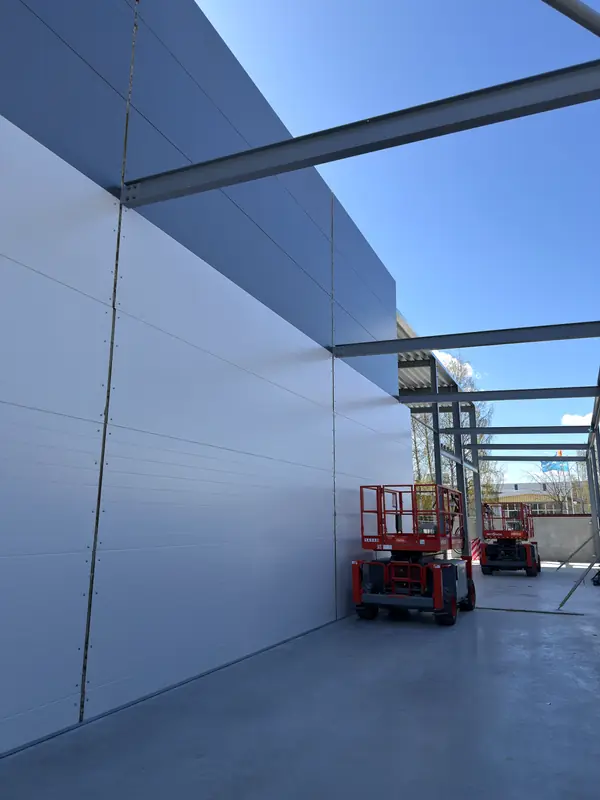 Tall white sandwich-panel wall during installation in Jönköping