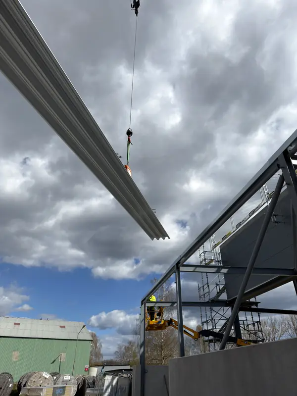 Long profiled roof sheets being lifted by crane over the steel frame
