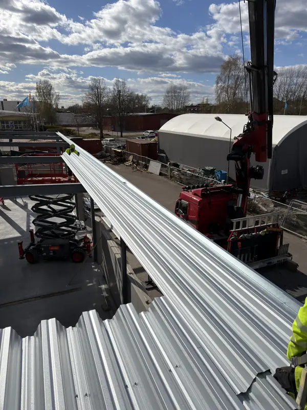 Installation crew positioning a long profiled roof-deck section