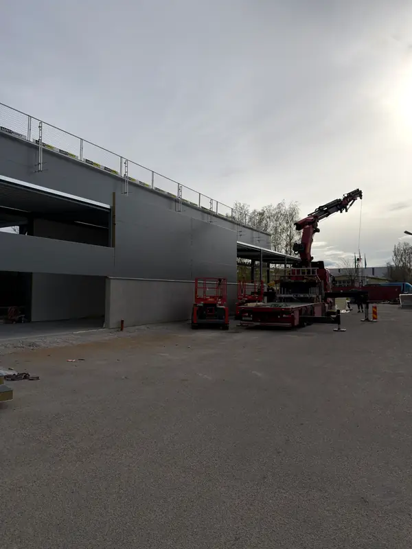 Grey sandwich-panel façade being enclosed with crane support