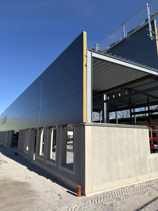 Grey sandwich wall panels meeting the covered roof section at a building corner
