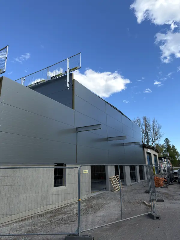 Long grey sandwich-panel façade nearing completion under a blue sky